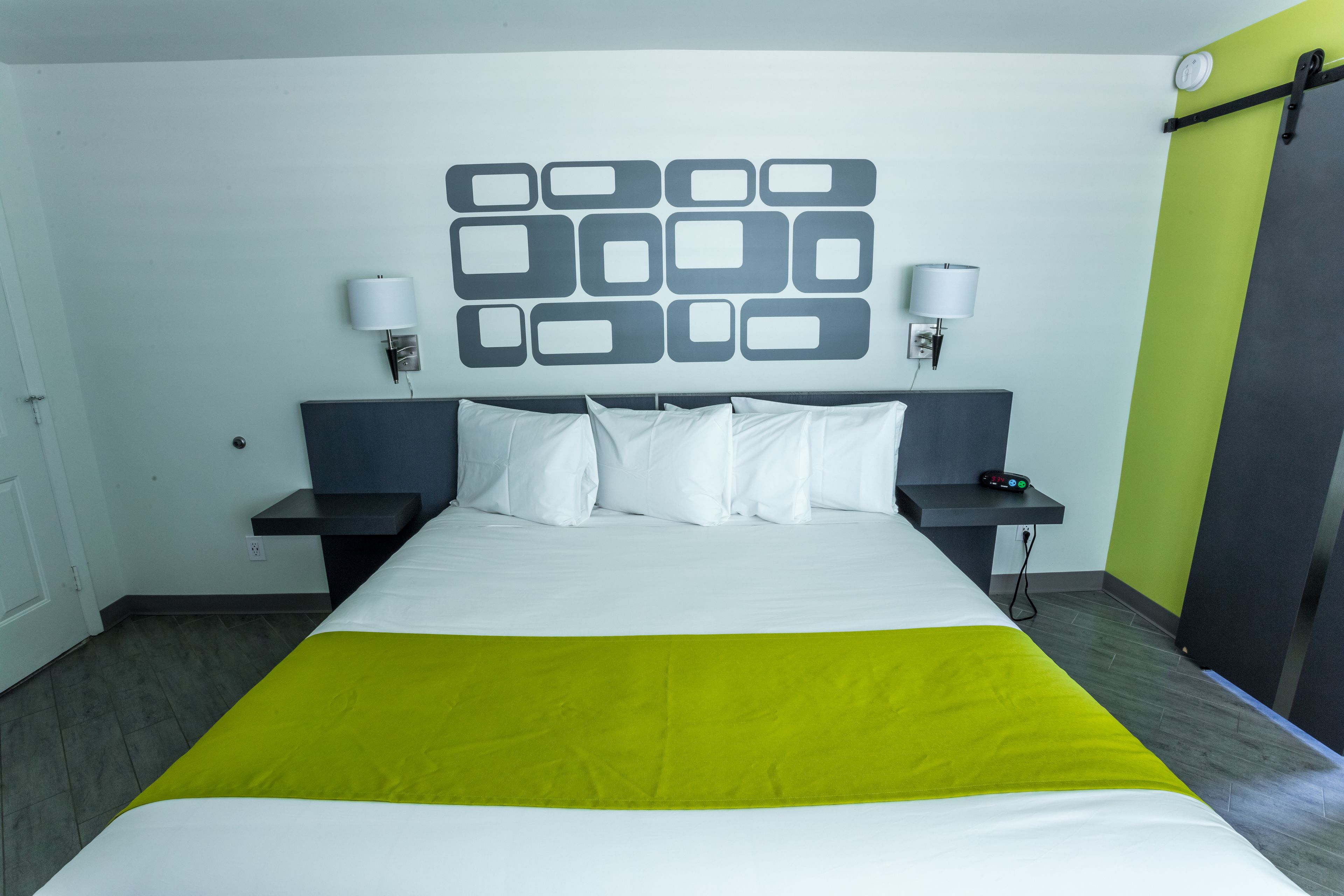 A hotel room with a bed, two bedside tables, a wall-mounted lamp, and a green accent wall.