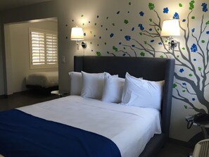 A neatly made bed with white linens and a blue throw blanket, a dark headboard, and wall-mounted lamps with floral wall decals.