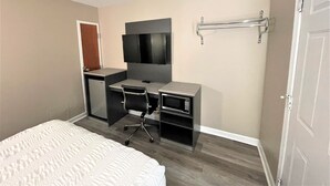 Ein Schlafzimmer mit Bett, Schreibtisch mit Computer, Fernseher und einer kleinen Küchenzeile.
