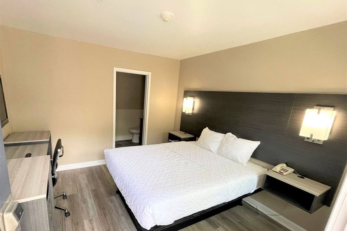 Habitación de hotel con cama, mesita de noche, lámpara y espejo.