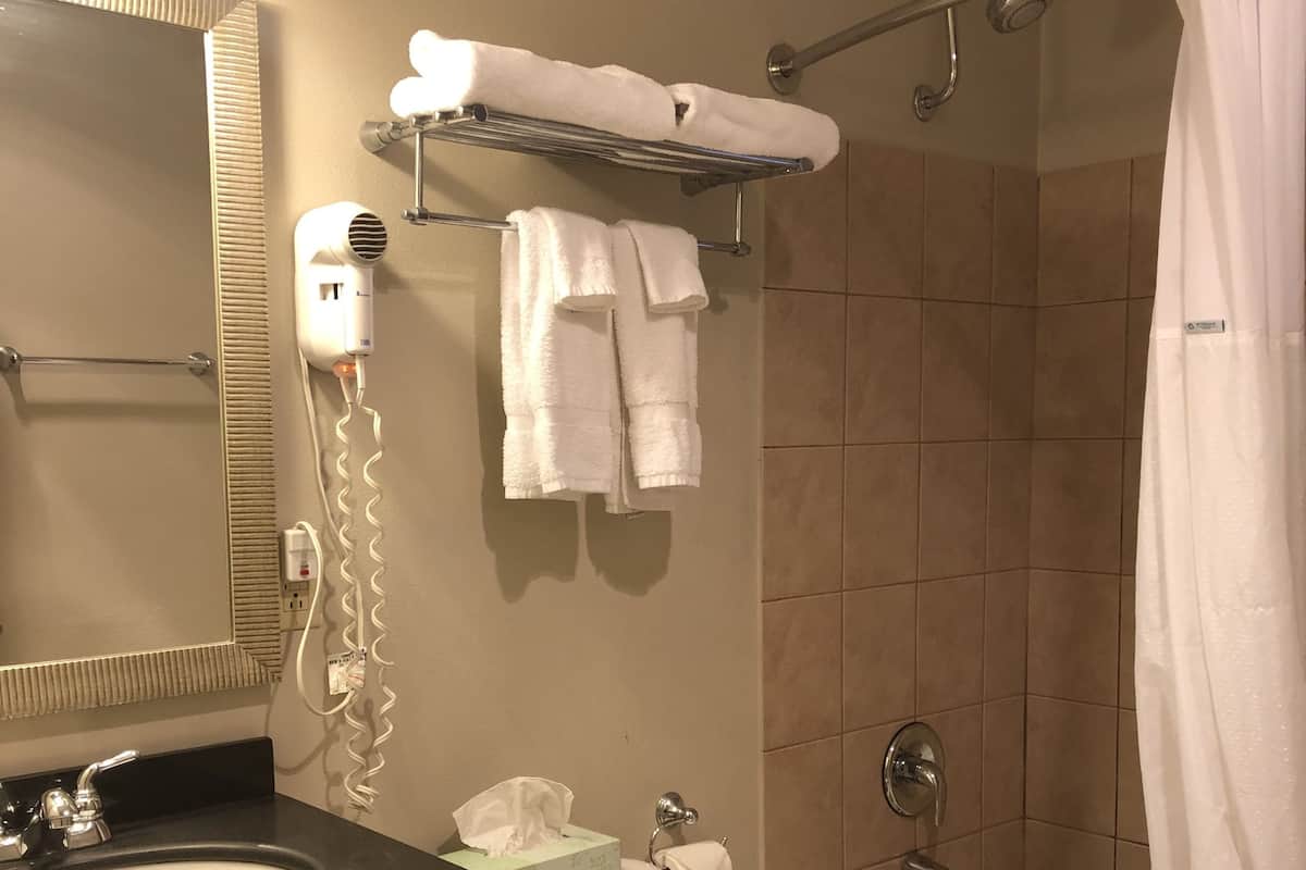 Ein Badezimmer mit Waschbecken, Toilette und Badewanne. Handtücher, ein Fön und ein Toilettenpapierhalter sind auf einem Handtuchhalter angebracht.