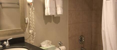 A bathroom with a sink, toilet, and bathtub. There is a towel rack with towels, a hairdryer, and a toilet paper holder.