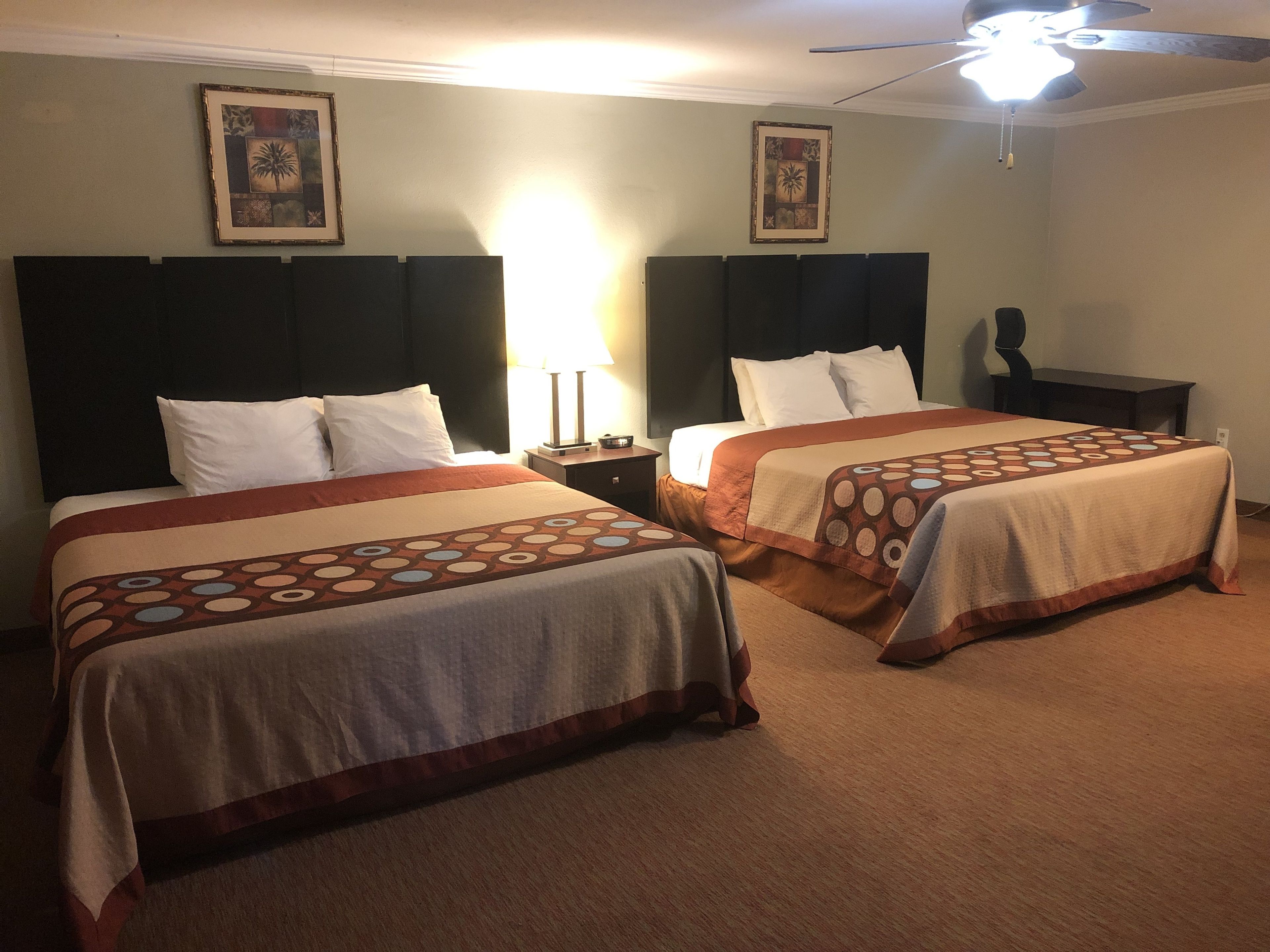 Two single beds with headboards, a nightstand, a lamp, and a ceiling fan in a hotel room.