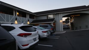 A parking lot with several cars parked in front of a building with a sloped roof and large windows. - Global INN (Coos Bay)