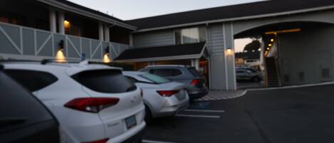 Un parking où plusieurs voitures sont garées devant un bâtiment doté d’un toit en pente et de grandes fenêtres.