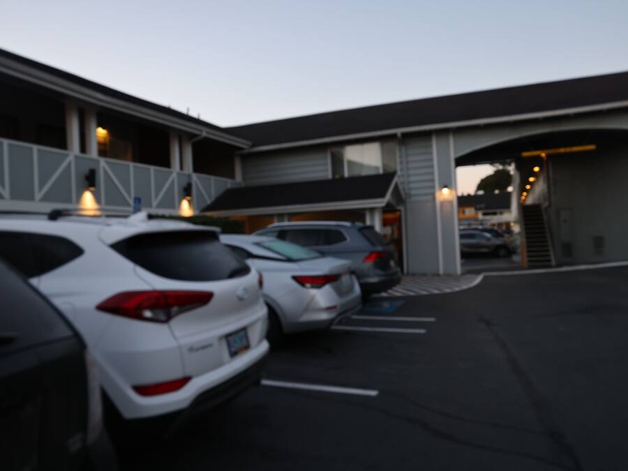 Un parking où plusieurs voitures sont garées devant un bâtiment doté d’un toit en pente et de grandes fenêtres.