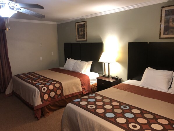 Habitación de hotel con dos camas, un ventilador de techo, una mesita de noche con lámpara y un cuadro en la pared.