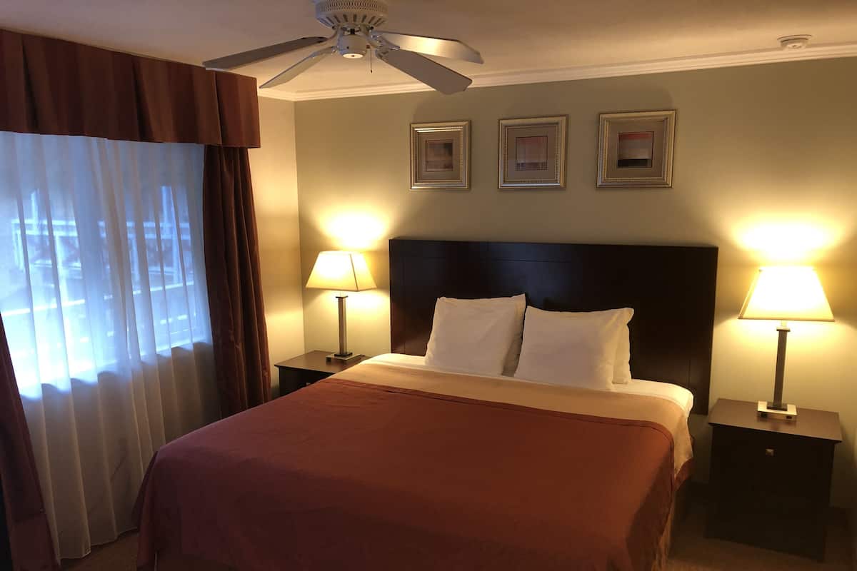 Ein Hotelzimmer mit einem Bett, zwei Nachttischen mit Lampen, einem Deckenventilator und drei gerahmten Bildern an der Wand.