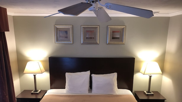 A hotel room with a large bed, two bedside lamps, a ceiling fan, and three framed pictures on the wall. - Global INN (Coos Bay)