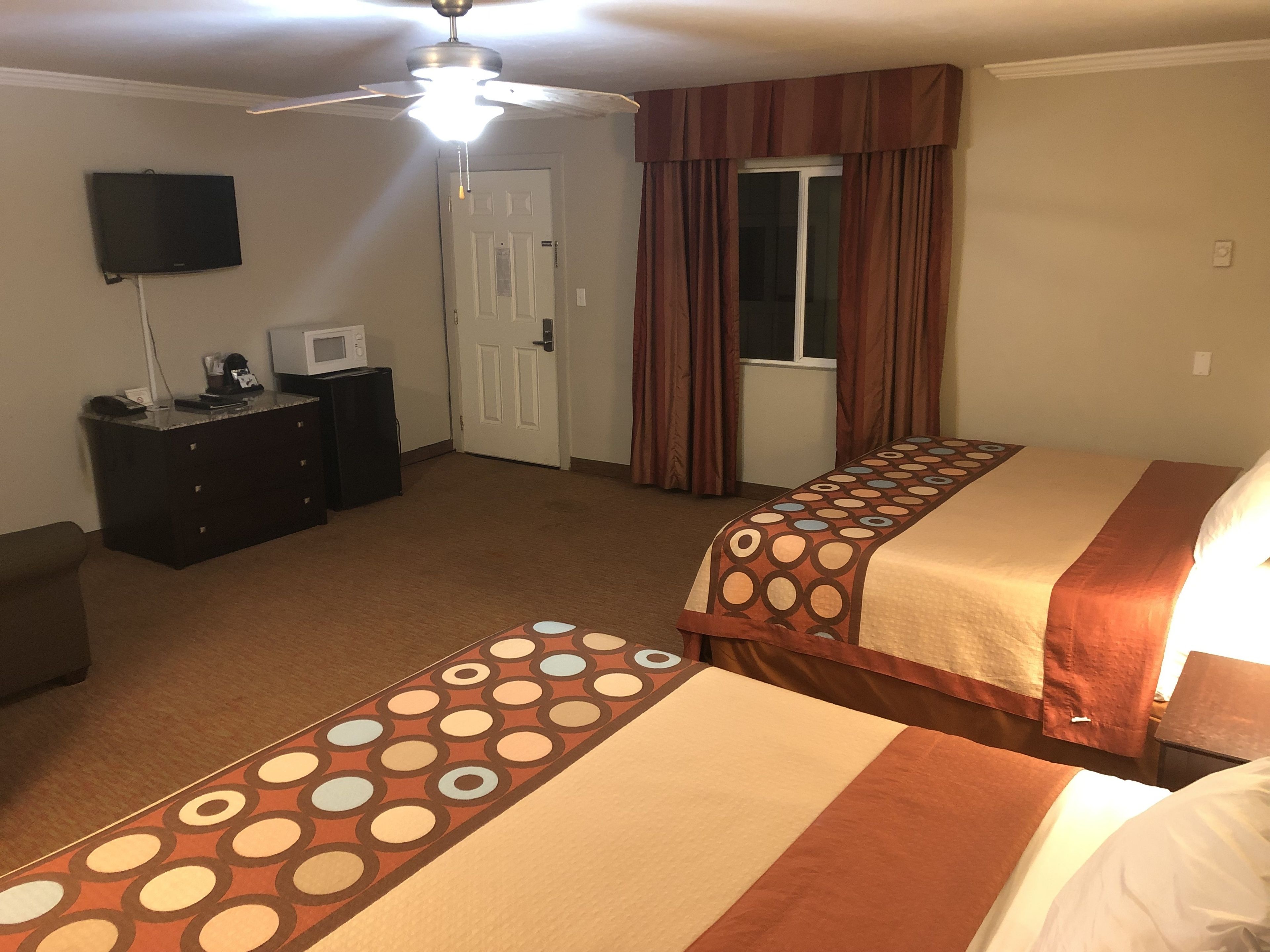 Una habitación de hotel con dos camas, un escritorio con una computadora, un microondas y un ventilador de techo.