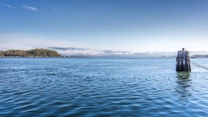 A calm lake with a wooden pier extending into the water, surrounded by a forested island and distant mountains. - Global INN (Coos Bay)