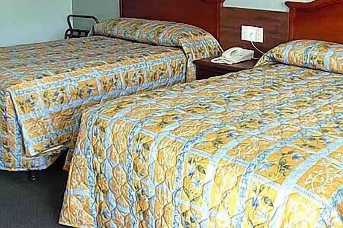 A hotel room with two single beds, a wooden headboard, a bedside table with a lamp, and a wall-mounted telephone.