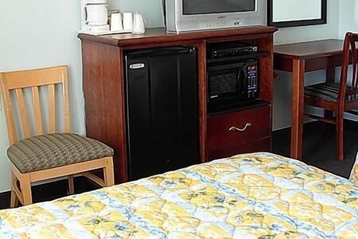 A small room with a bed, a wooden chair, a desk with a television, a coffee maker, and a microwave.