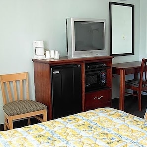 A small room with a bed, a wooden chair, a desk with a television, a coffee maker, and a microwave.