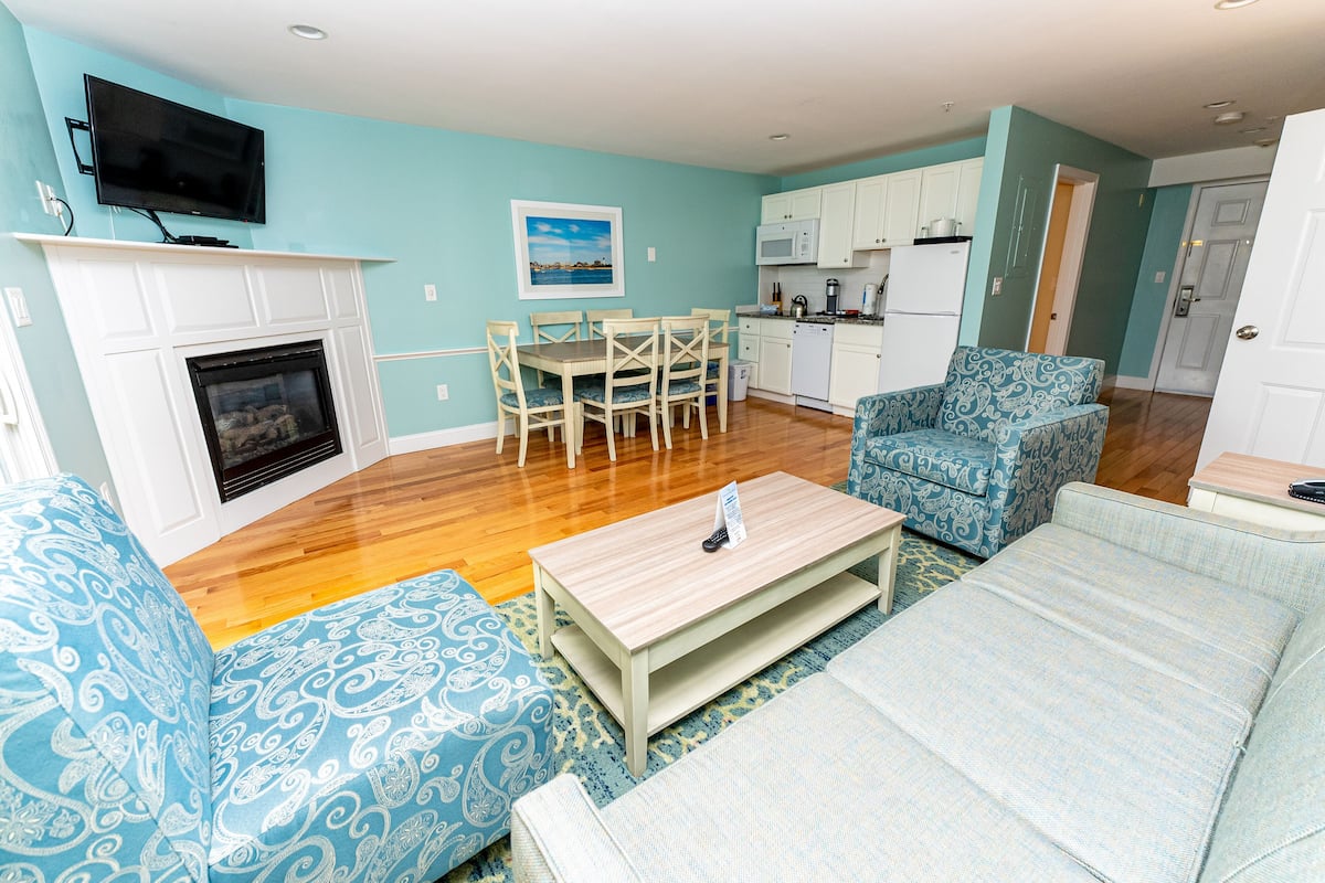 A living room with a fireplace, a dining table with chairs, a patterned armchair, and a sofa.