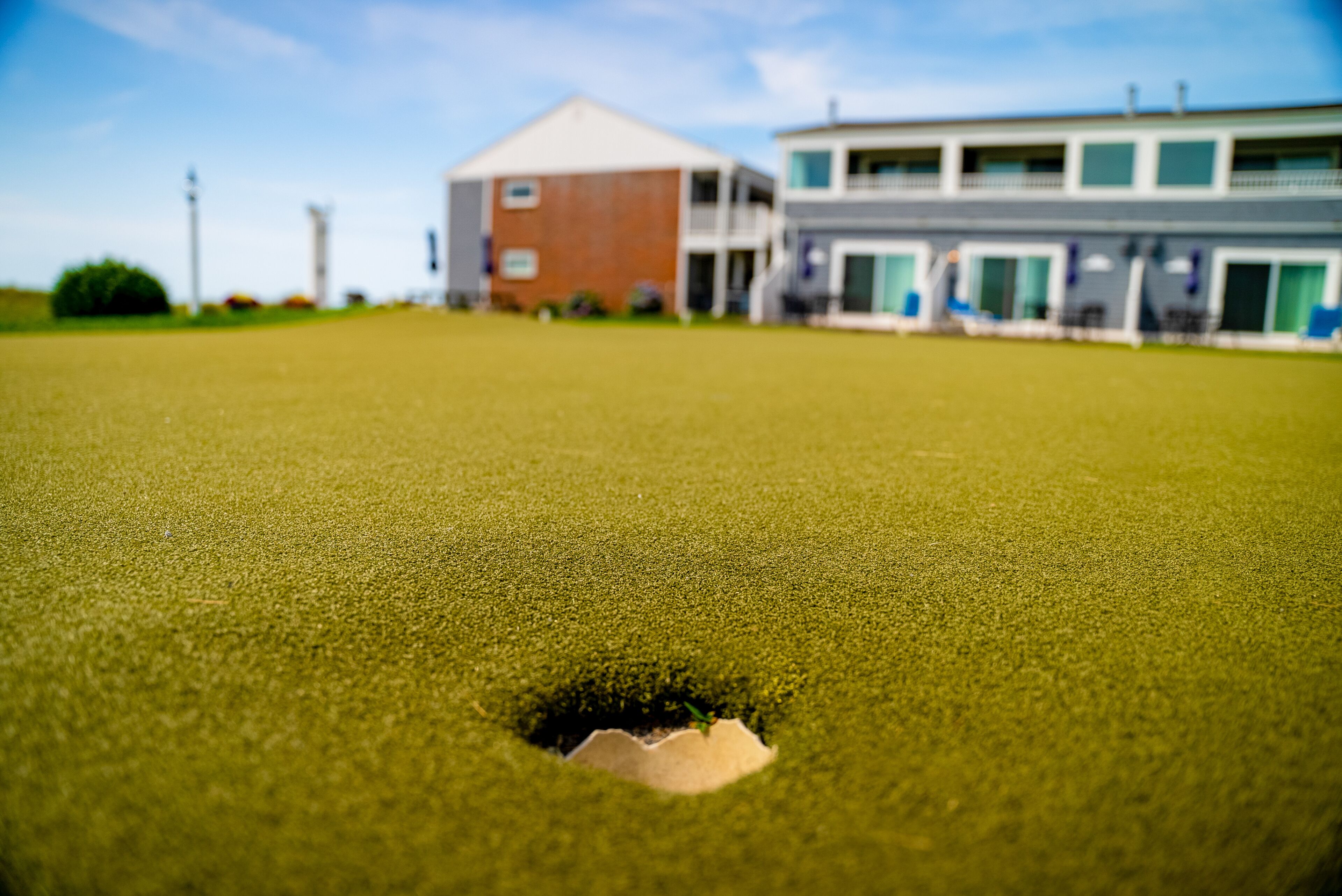 A grassy area with a hole, a building with a flat roof, and a modern structure with large windows.