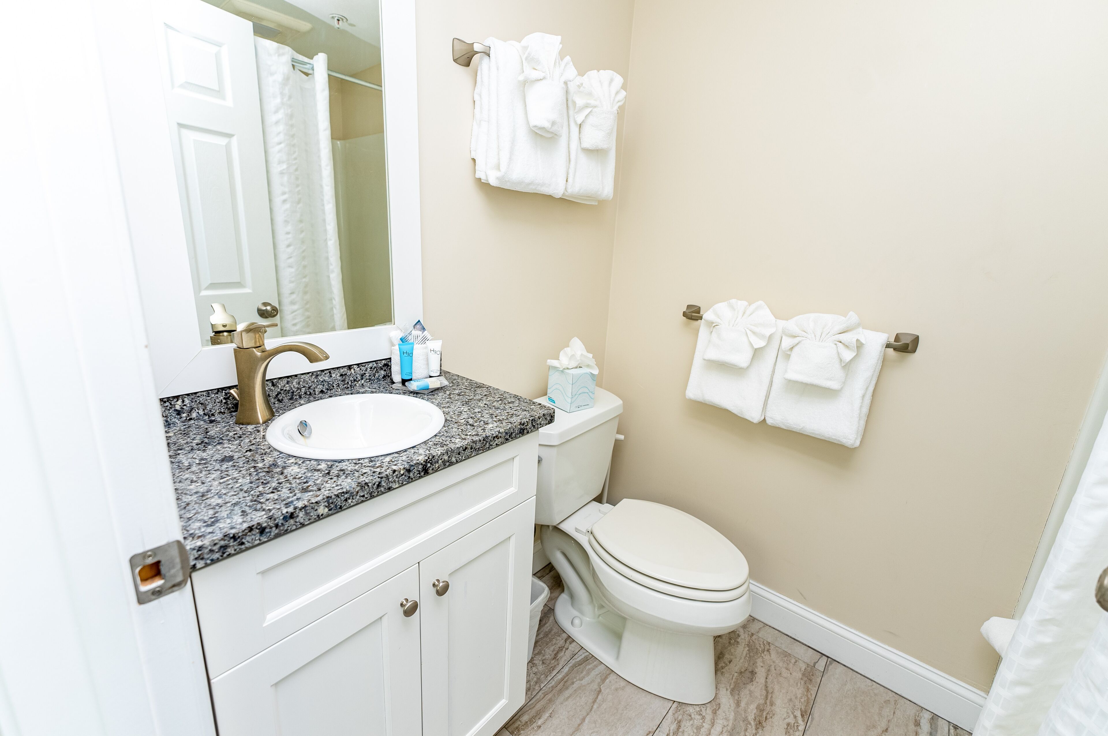A bathroom with a white sink, vanity, and toilet. There are towels hanging on the wall and a shower curtain.