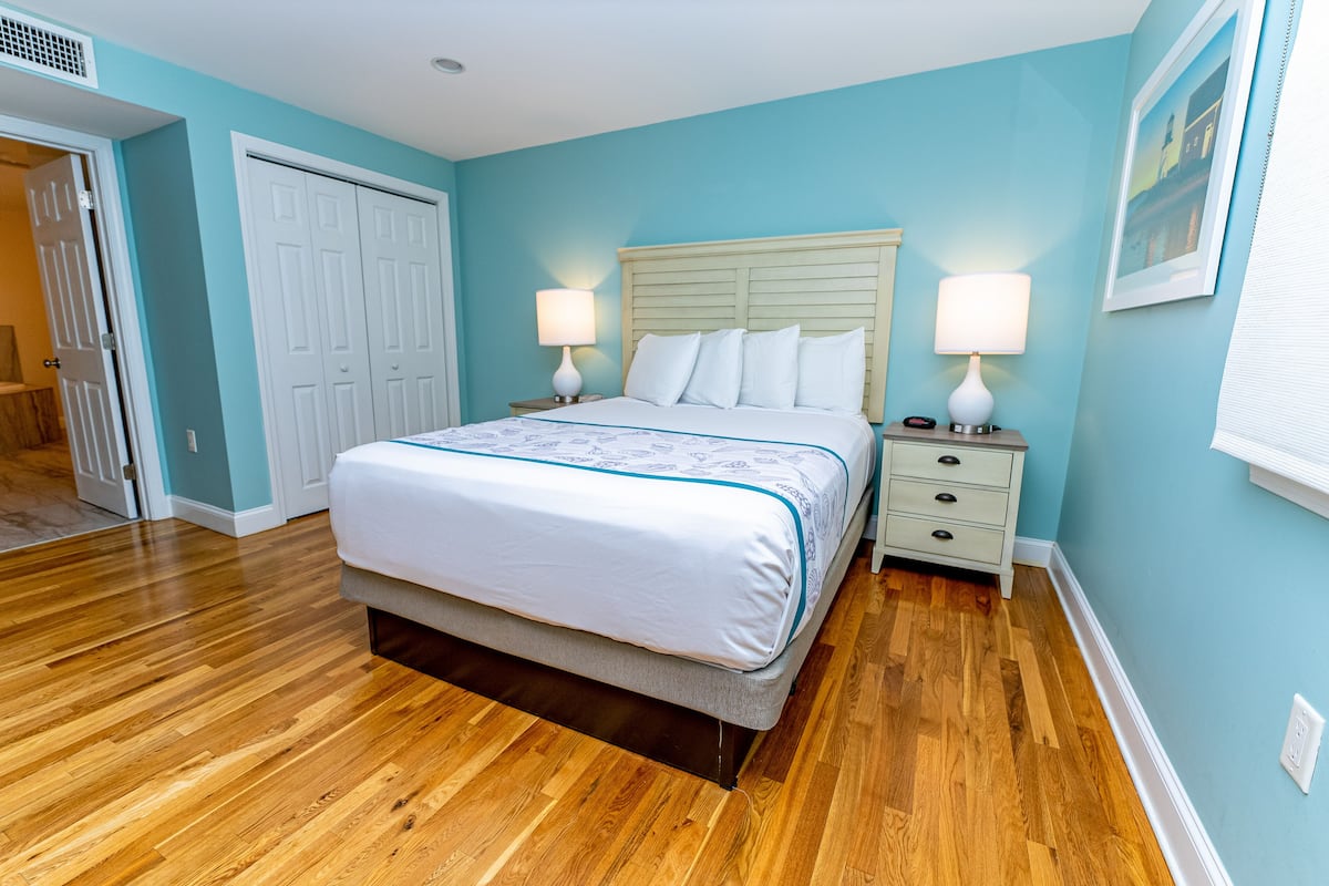A bedroom with a bed, two bedside tables, a nightstand, a door, and a wall with a picture.