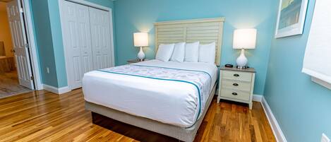 A bedroom with a bed, two bedside tables, a nightstand, a door, and a wall with a picture.
