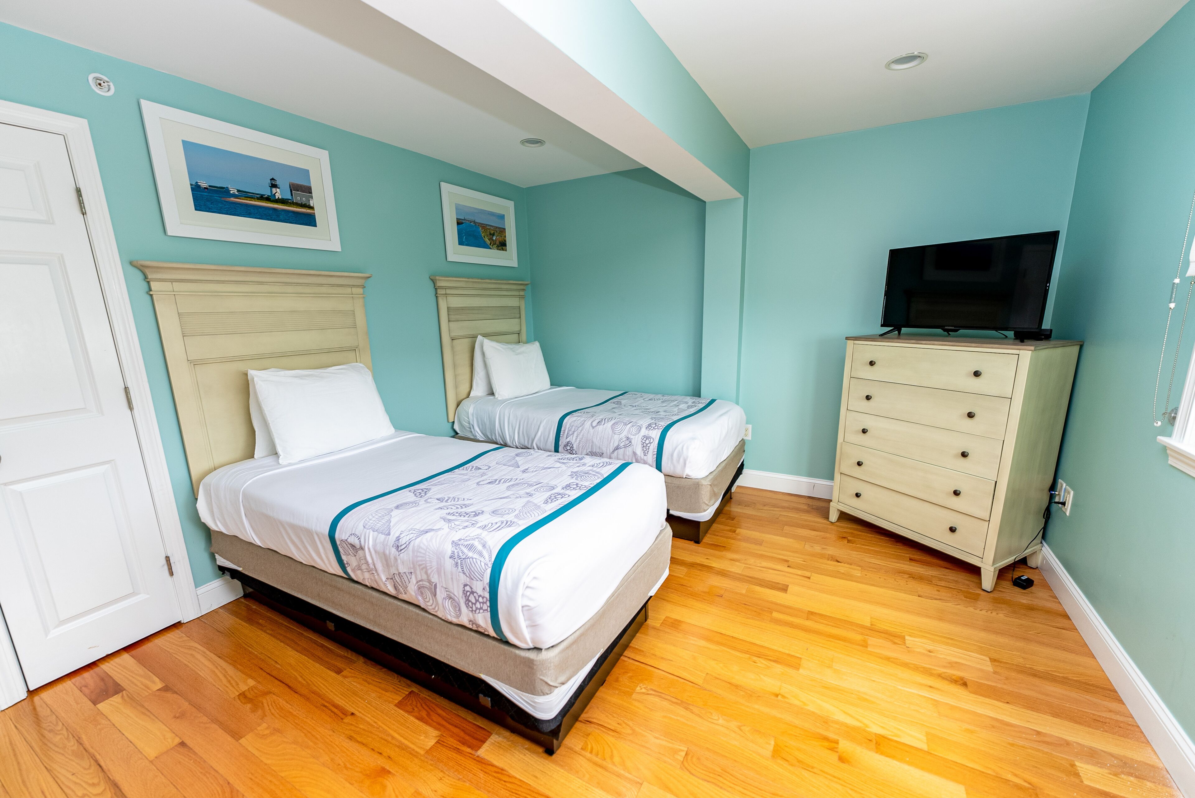 A bedroom with two beds, a dresser, and a television.