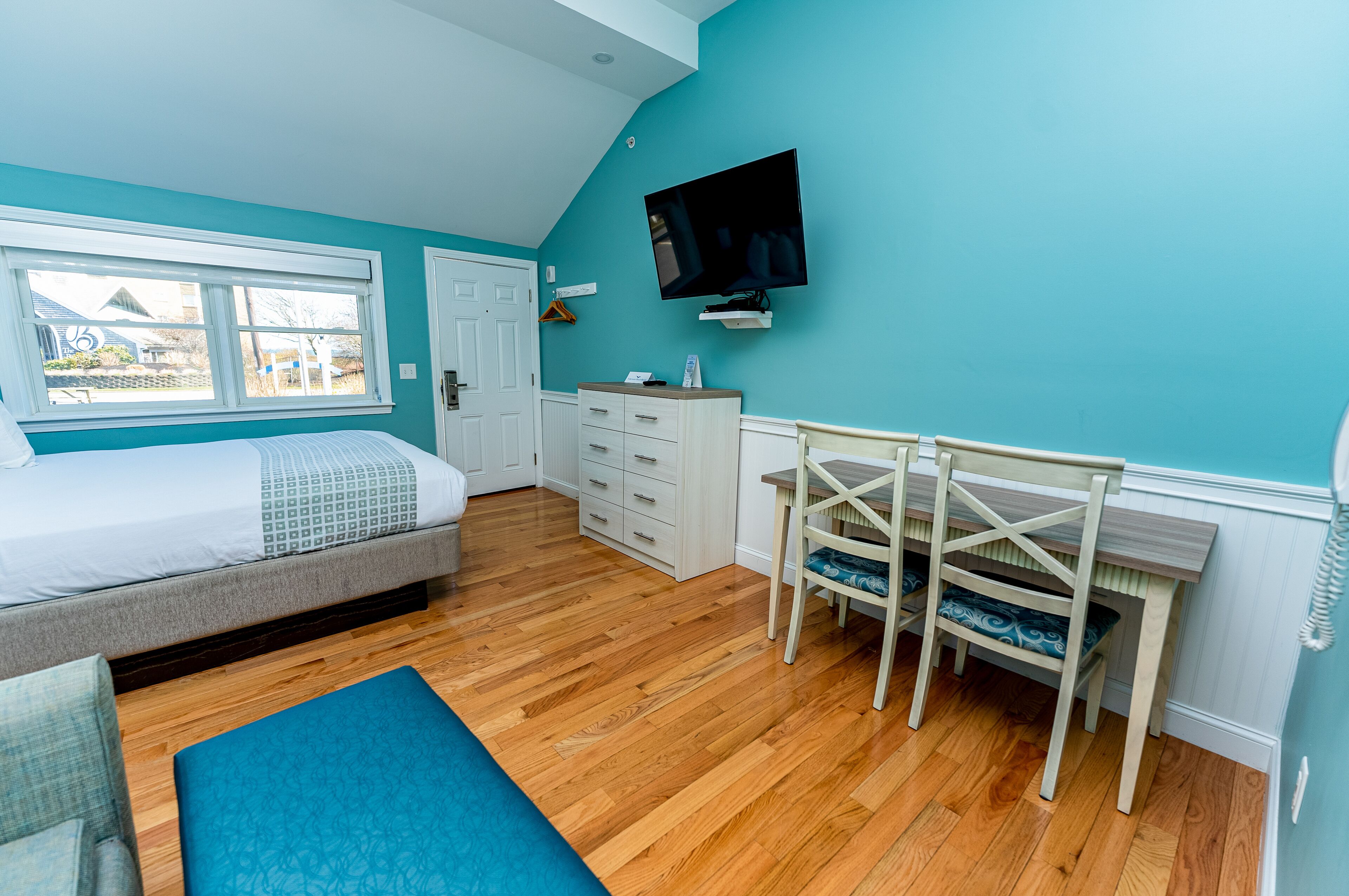 Une chambre à coucher avec un lit, un bureau, une chaise, une télévision et une fenêtre.