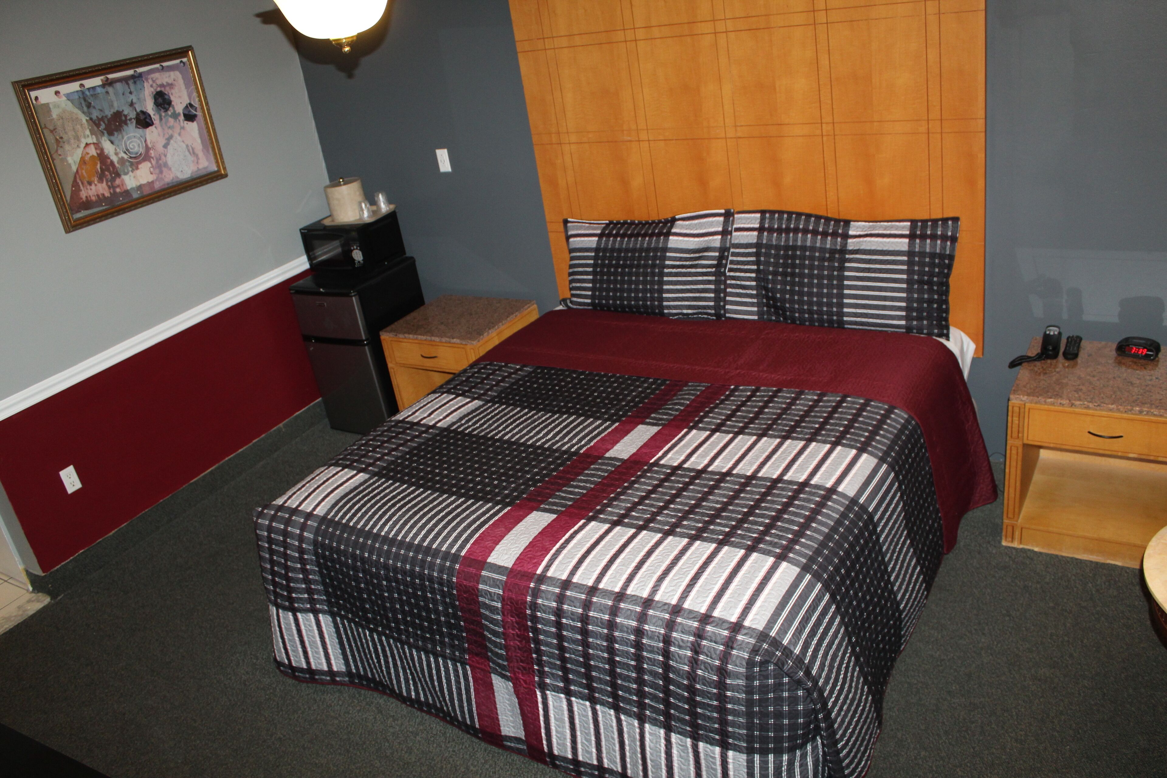 Una habitación de hotel con una cama grande, cabecera de madera, mesita de noche, escritorio y lámpara de pared.