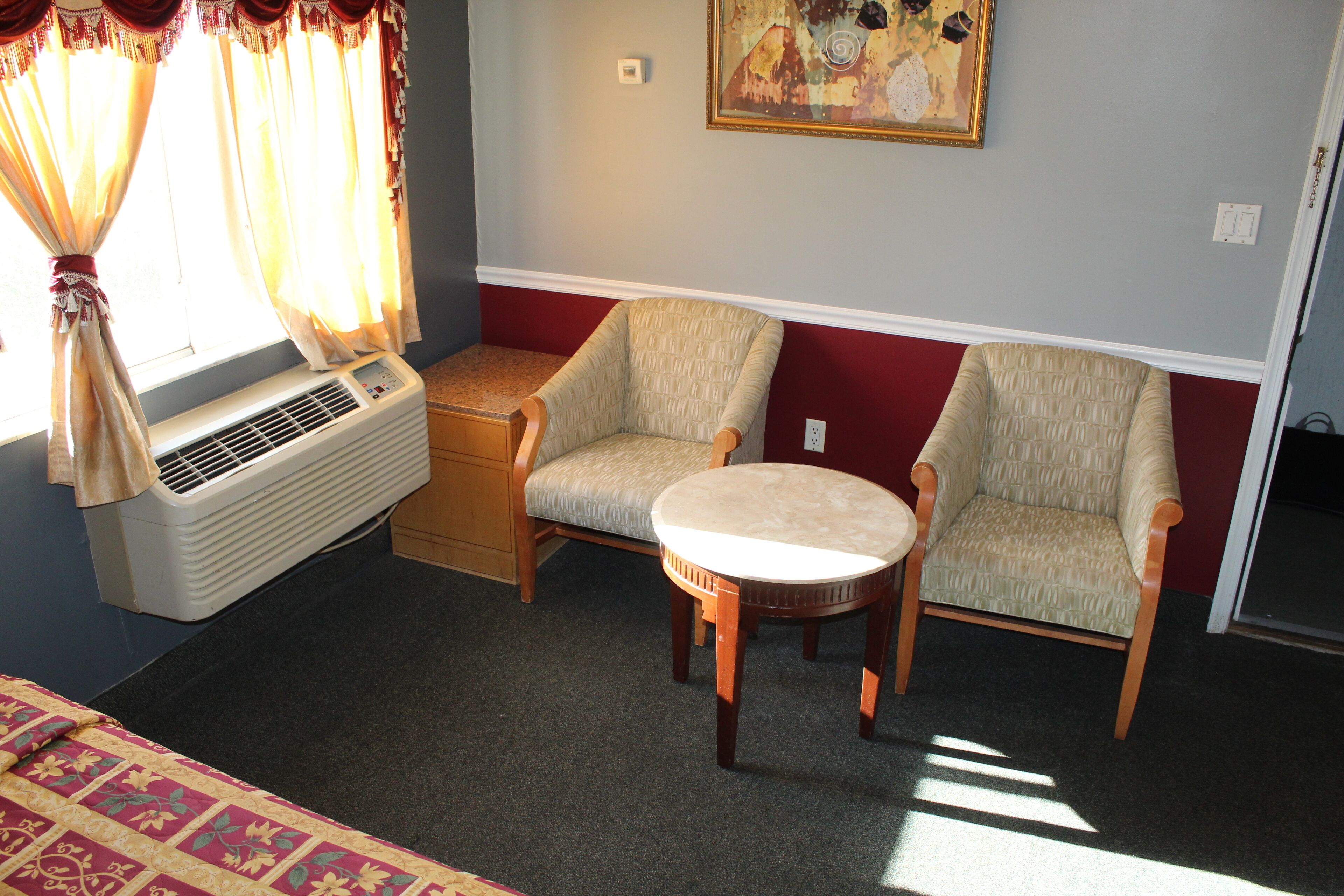 A room with two armchairs, a small table, a window with curtains, and a wall-mounted air conditioner.