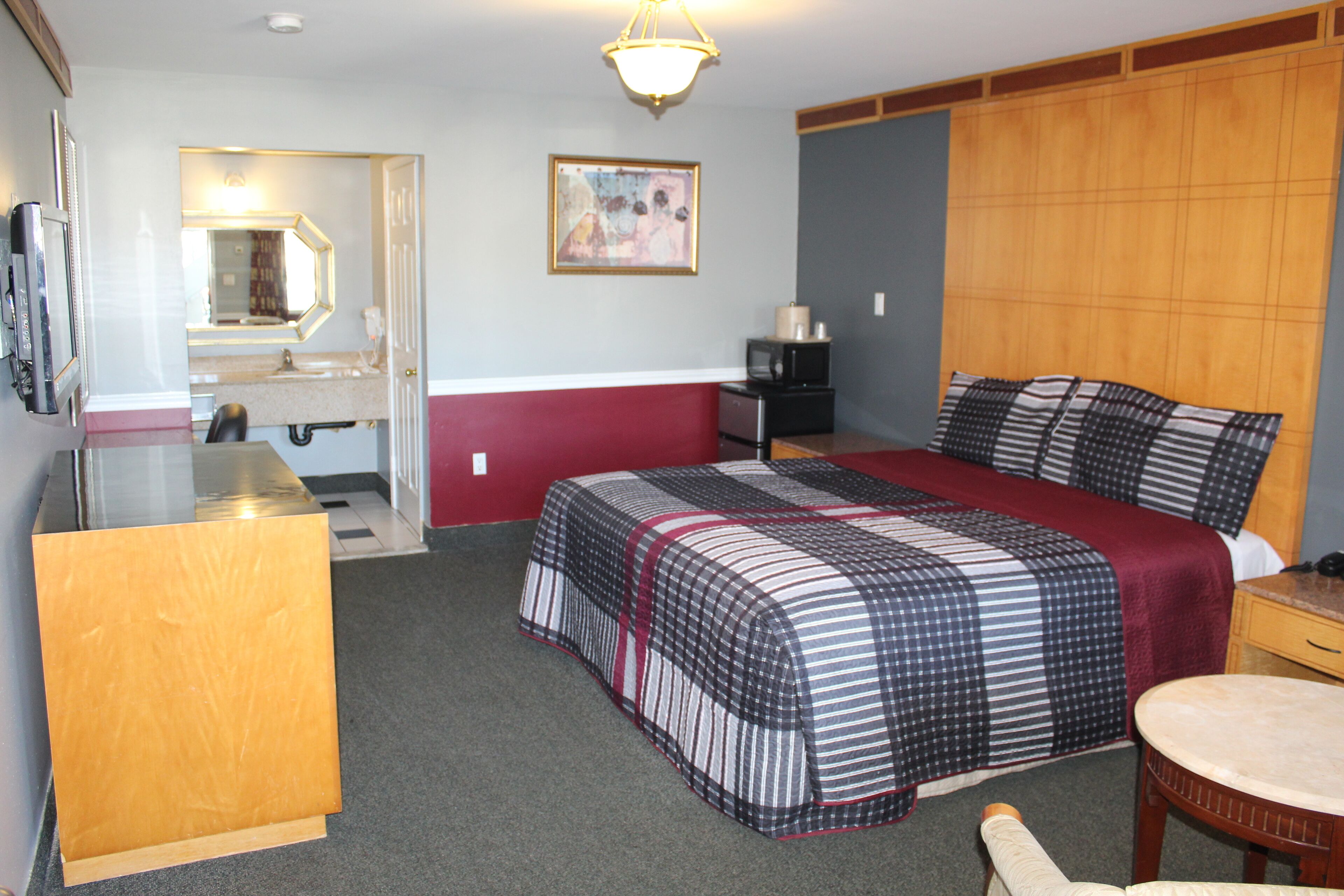 A hotel room with a bed, a desk, a chair, a television, a mirror, and a painting on the wall.