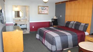 A hotel room with a bed, a desk, a chair, a television, a mirror, and a painting on the wall.