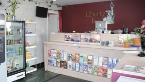 A reception desk with a Liberty Inn sign, a refrigerator stocked with beverages, and a display of travel brochures. - Liberty Inn Atlantic City (Absecon)