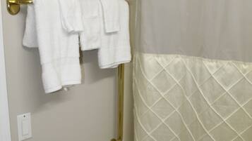 A bathroom with a gold towel rack holding two white towels, a shower curtain, and a small green bottle on the wall.