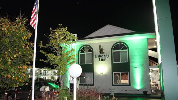 A Liberty Inn building at night with green lighting, an American flag, and a well-maintained garden area. - Liberty Inn Atlantic City (Absecon)