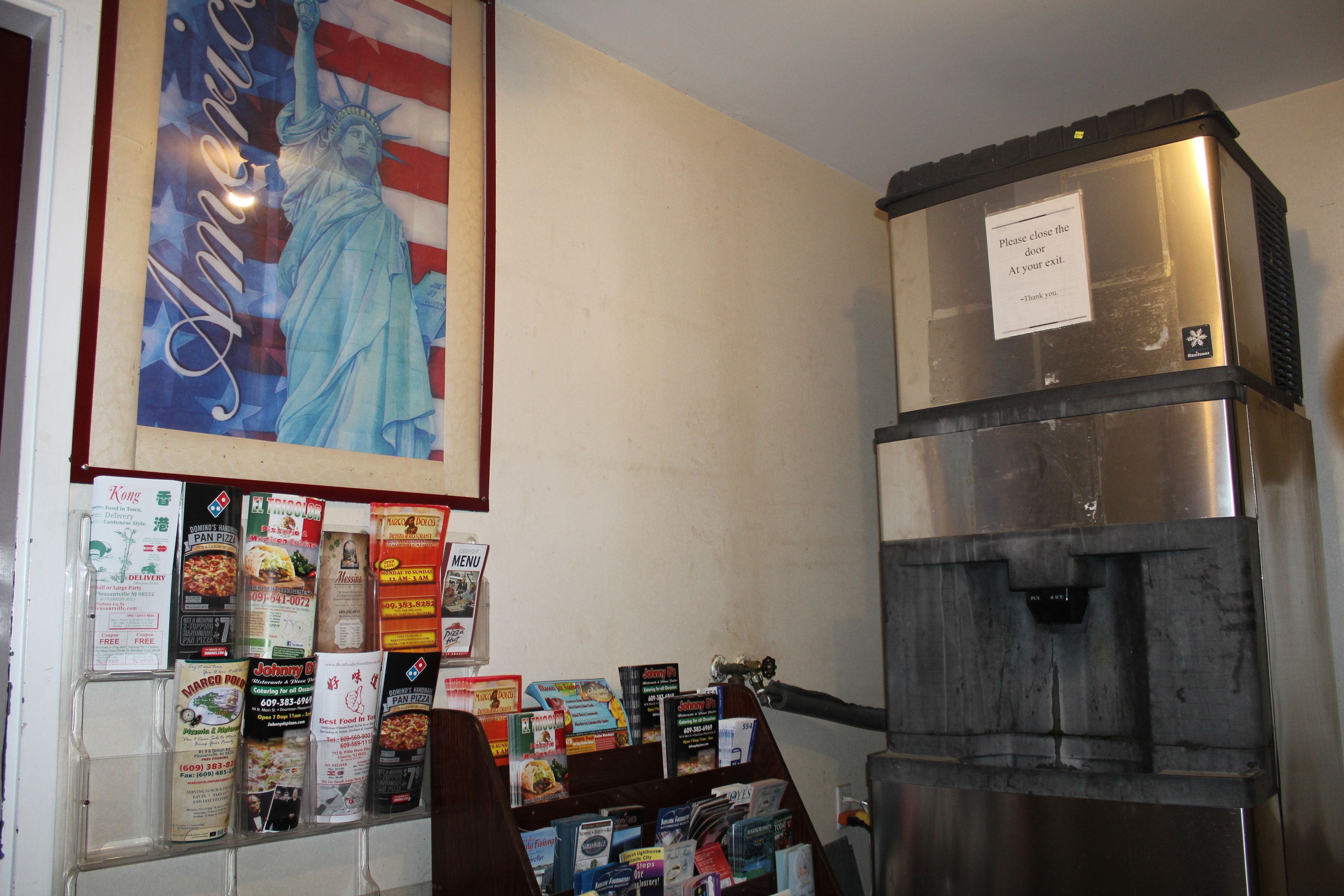 Un muro con una bandiera americana incorniciata e un poster della Statua della Libertà. In basso, diversi volantini e un grande elettrodomestico, probabilmente un frigorifero.
