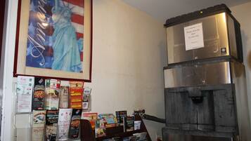 Un muro con una bandiera americana incorniciata e un poster della Statua della Libertà. In basso, diversi volantini e un grande elettrodomestico, probabilmente un frigorifero.