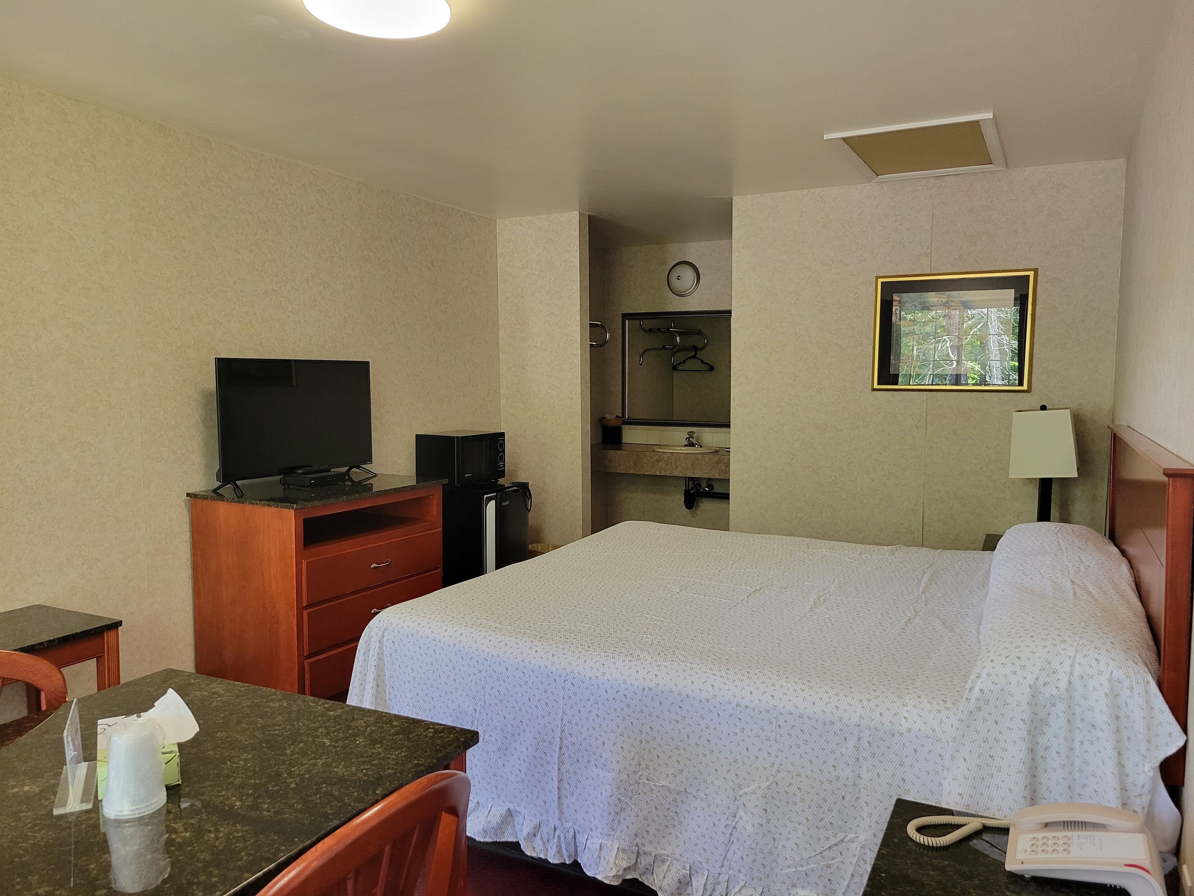 Ein Hotelzimmer mit einem Bett, einem Schreibtisch mit Computer, einem Fernseher, einer kleinen Minibar, einer Lampe und einem Telefon.
