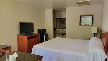 Ein Hotelzimmer mit einem Bett, einem Schreibtisch mit Computer, einem Fernseher, einer kleinen Minibar, einer Lampe und einem Telefon.