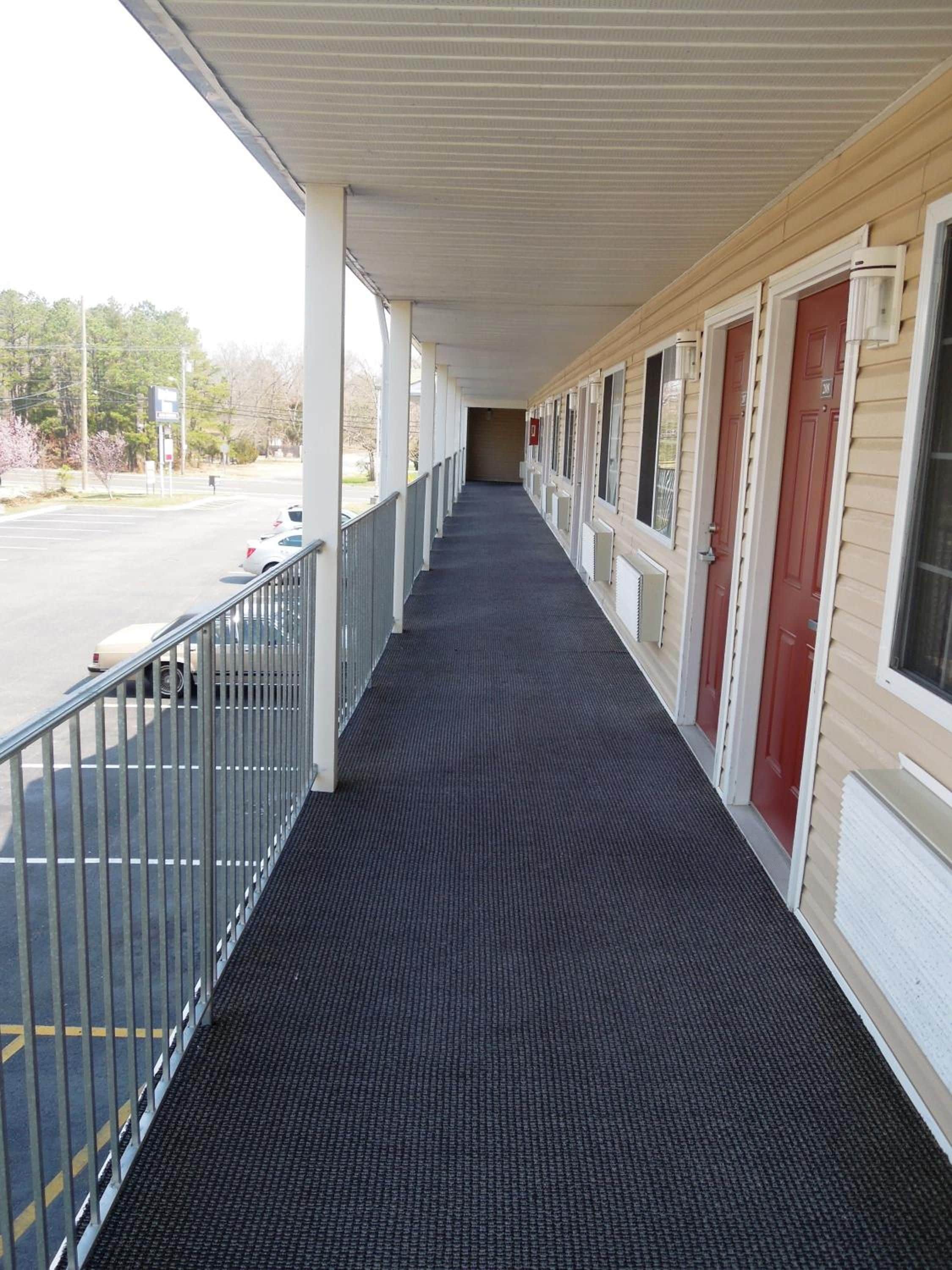 A covered corridor with a metal railing, leading to a row of doors with a red accent.