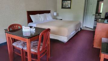 A hotel room with a bed, a desk with chairs, a framed picture on the wall, and a door leading to the kitchen.