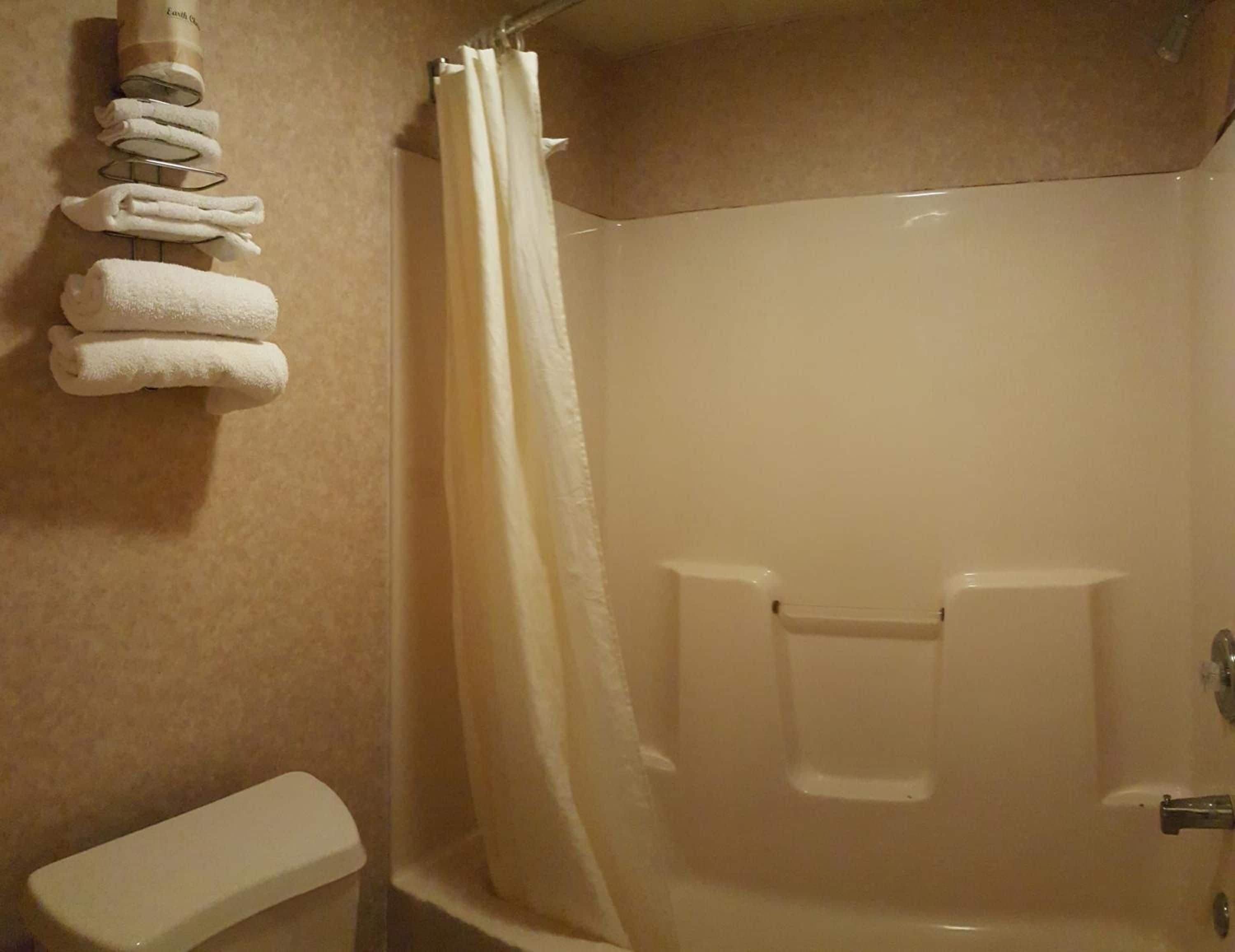 A bathroom with a shower, a toilet, and a towel rack with folded towels.