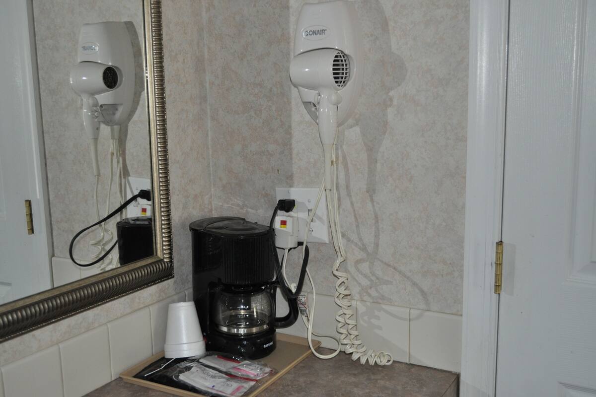 A bathroom with a hair dryer, a coffee maker, and a mirror.