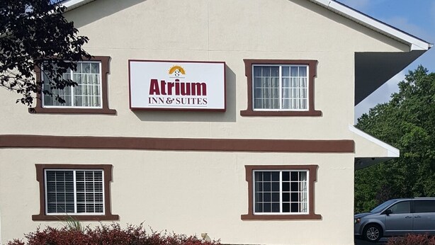 A two-story Atrium Inn & Suites building with a beige exterior, multiple windows, and a landscaped garden with various plants and flowers.