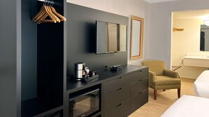 Una habitación de hotel moderna con un aparador de color oscuro, microondas, cafetera y una silla.