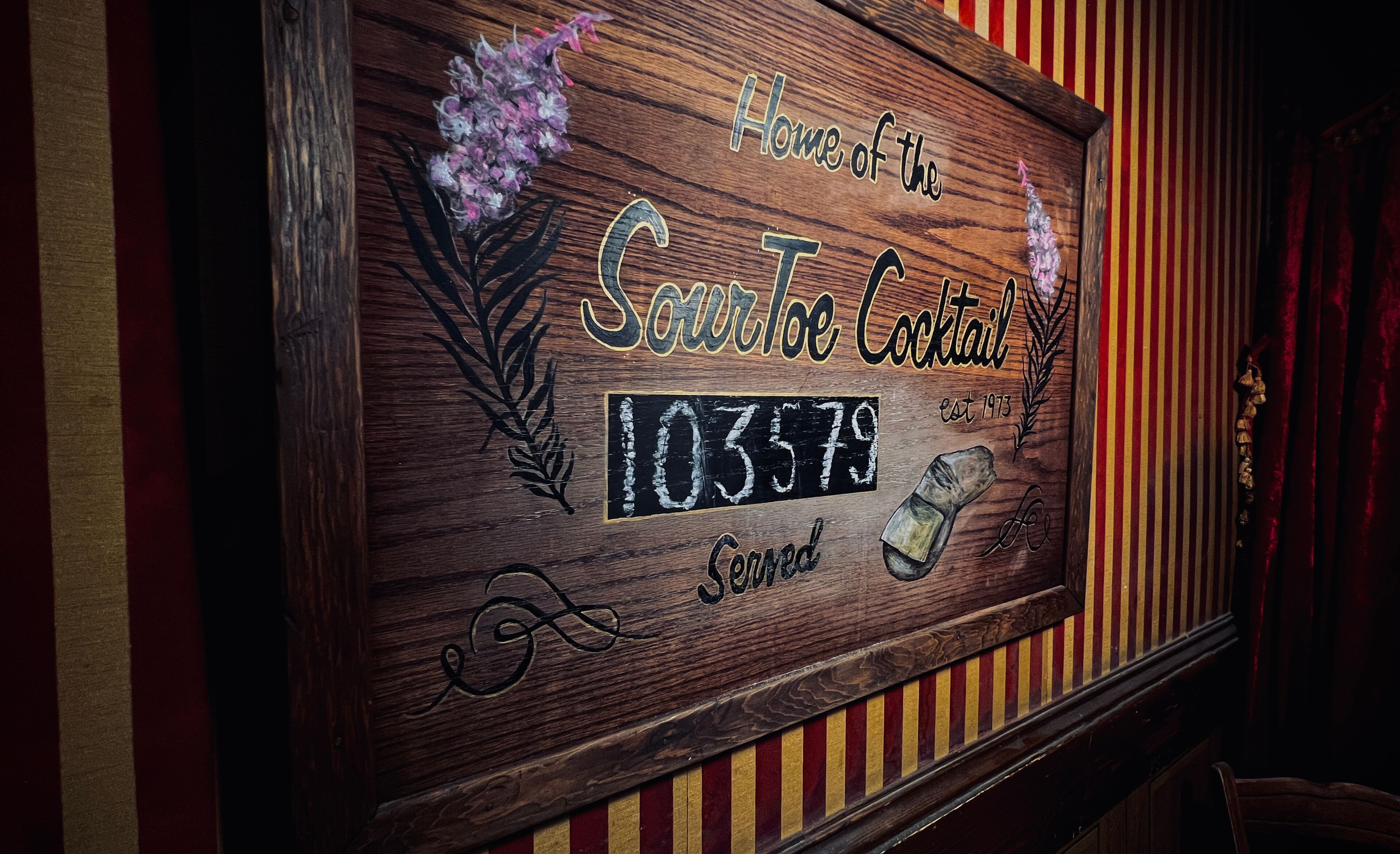 A wooden sign with the text "Home of the Sourtoe Cocktail" and the number "103579".