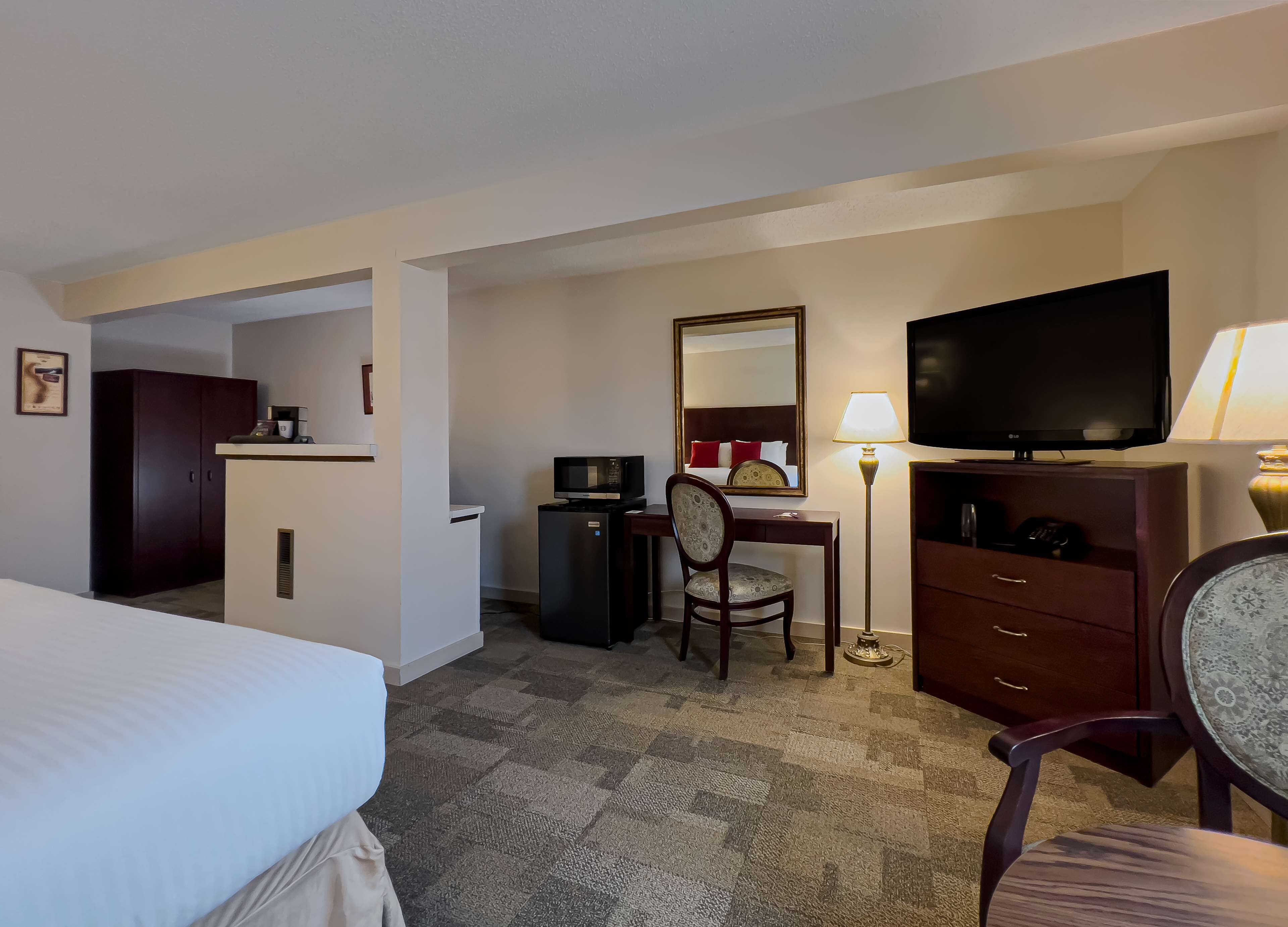 A hotel room with a bed, a desk with a chair, a television, a desk lamp, a wardrobe, and a microwave.