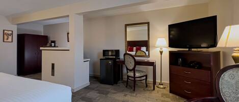A hotel room with a bed, a desk with a chair, a television, a desk lamp, a wardrobe, and a microwave.