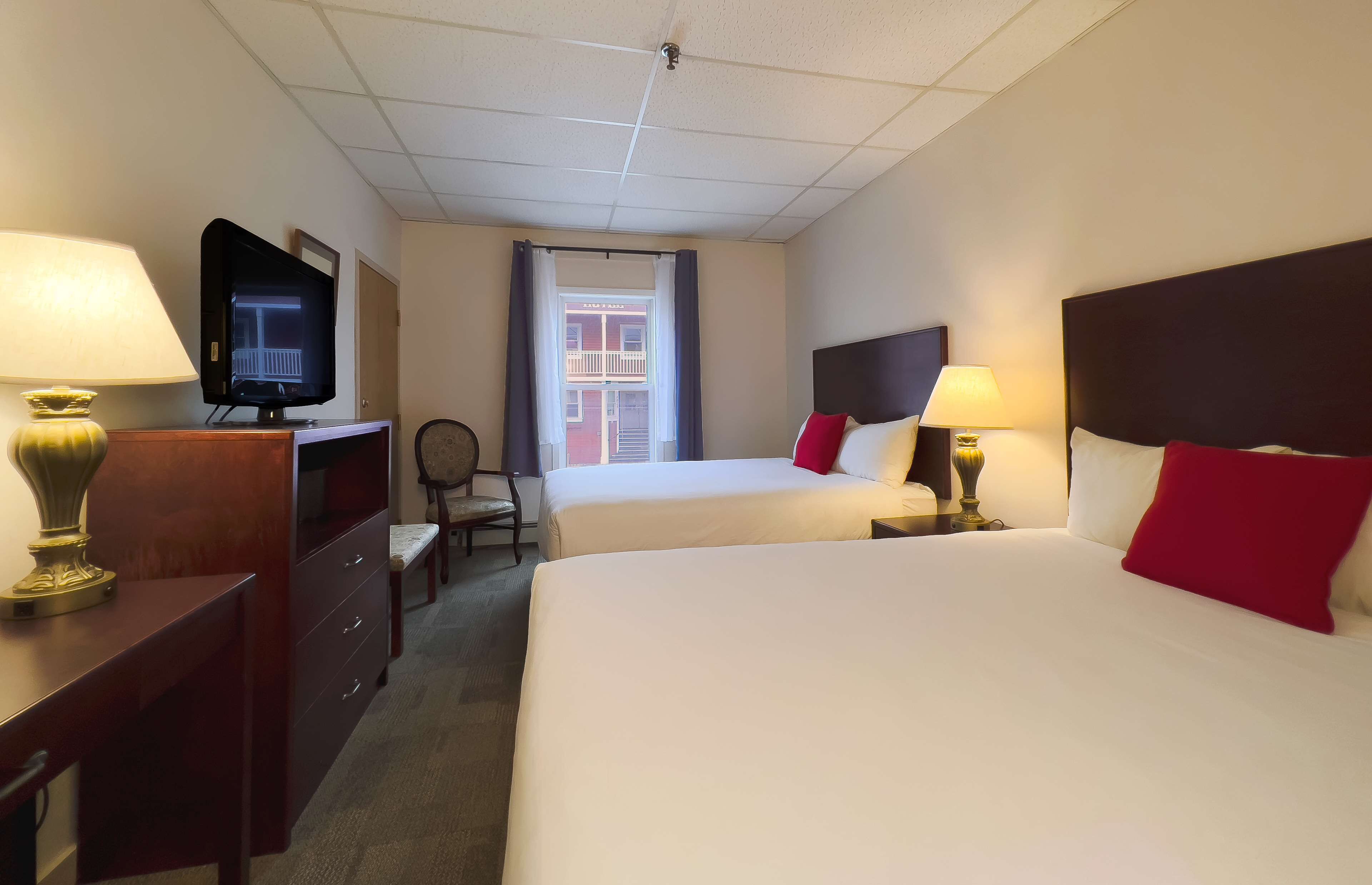 A hotel room with two beds, a TV, a desk with a lamp, and a chair.