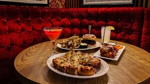 Una mesa redonda con diversos alimentos, como pizza, una hamburguesa y papas fritas, acompañada de un martini y una limonada.