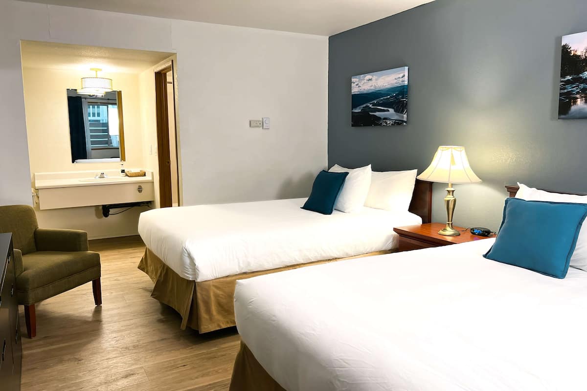 Una habitación de hotel con dos camas, un escritorio, una silla, una lámpara y un cuadro en la pared.