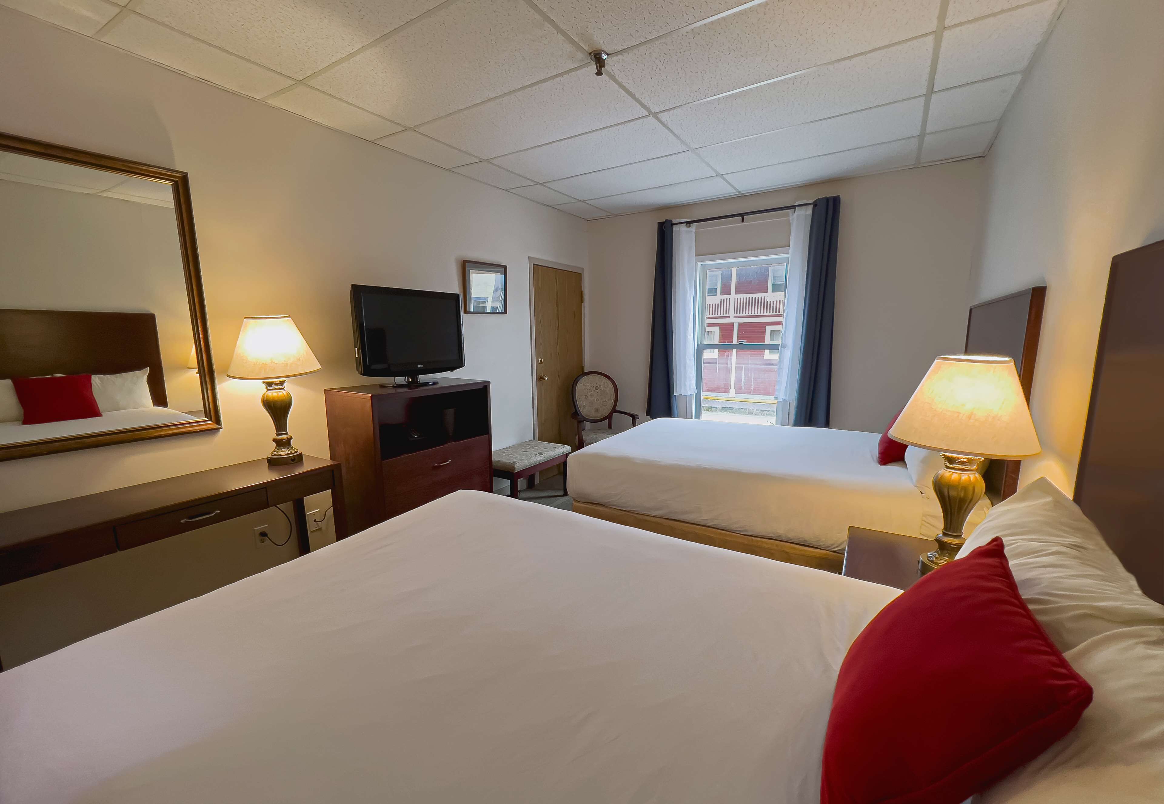 A hotel room with two beds, a television, a desk with a lamp, and a window with curtains.