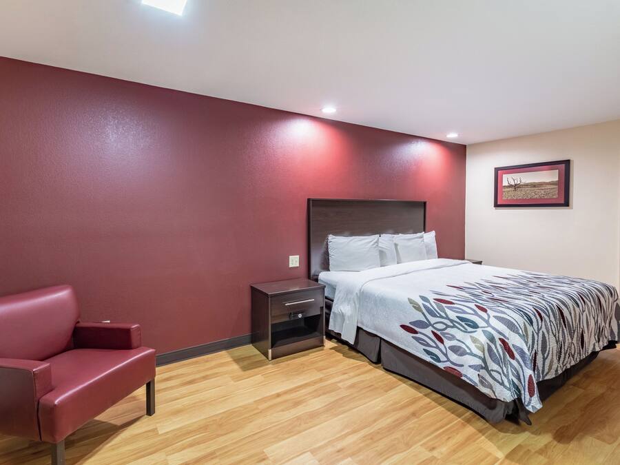 Une chambre d’hôtel avec un lit, une table de chevet, un fauteuil rouge et un tableau accroché au mur.